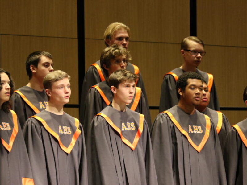 Ames High's choir sings in black robes with orange trim and orange letters that read AHS.