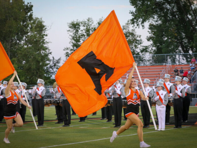 cheerleader runs on football field with a flag with an A on it