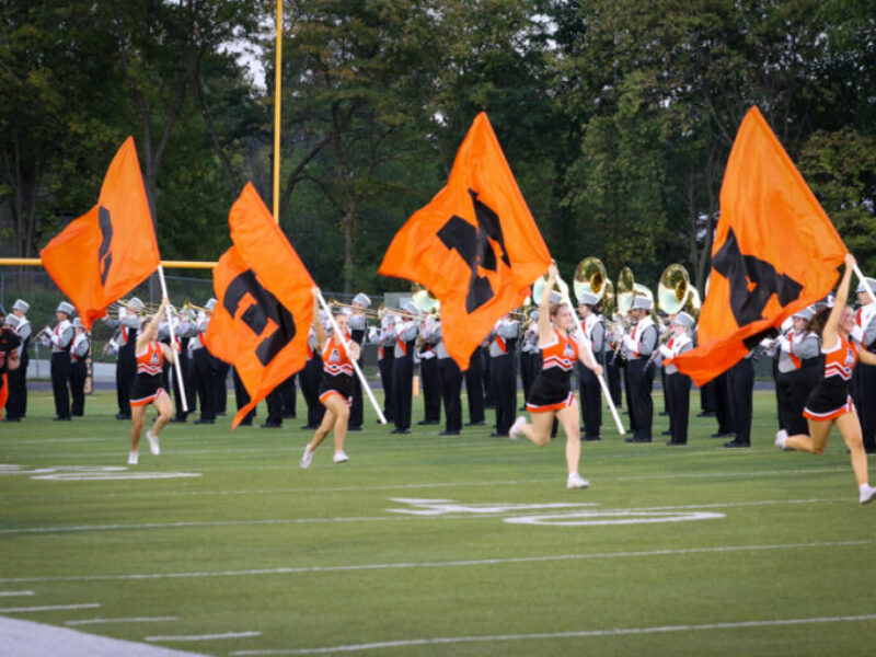 Cheerleaders run onto the football field with Ames flags