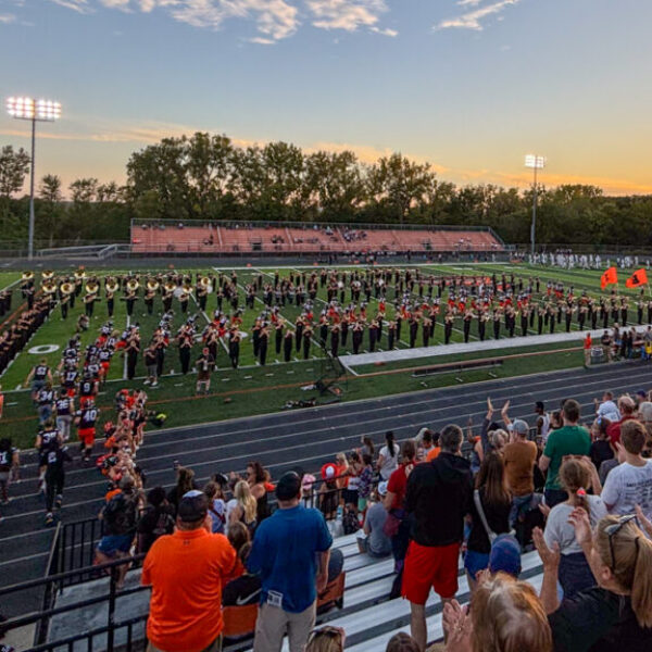 Marching band playing during the homecoming game while the football team runs out on the field with the cheerleaders.