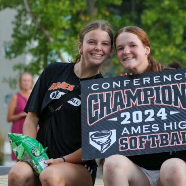 Two students who play Ames High softball smile and hold a sign during the homecoming parade